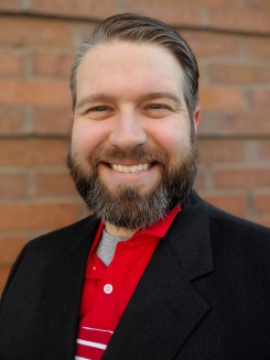 Headshot smiling bearded man with red shirt and dark blazer