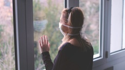 a woman standing at a window with a mask on.