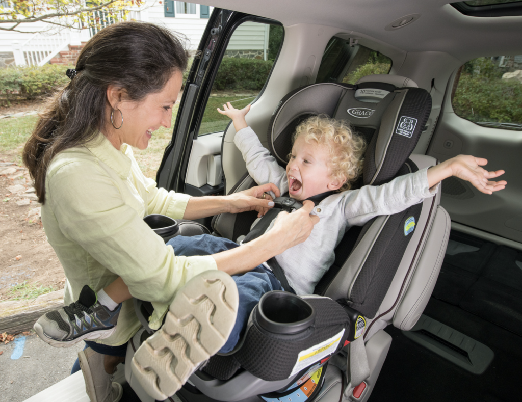 mom putting child in car seat and the child is excited 