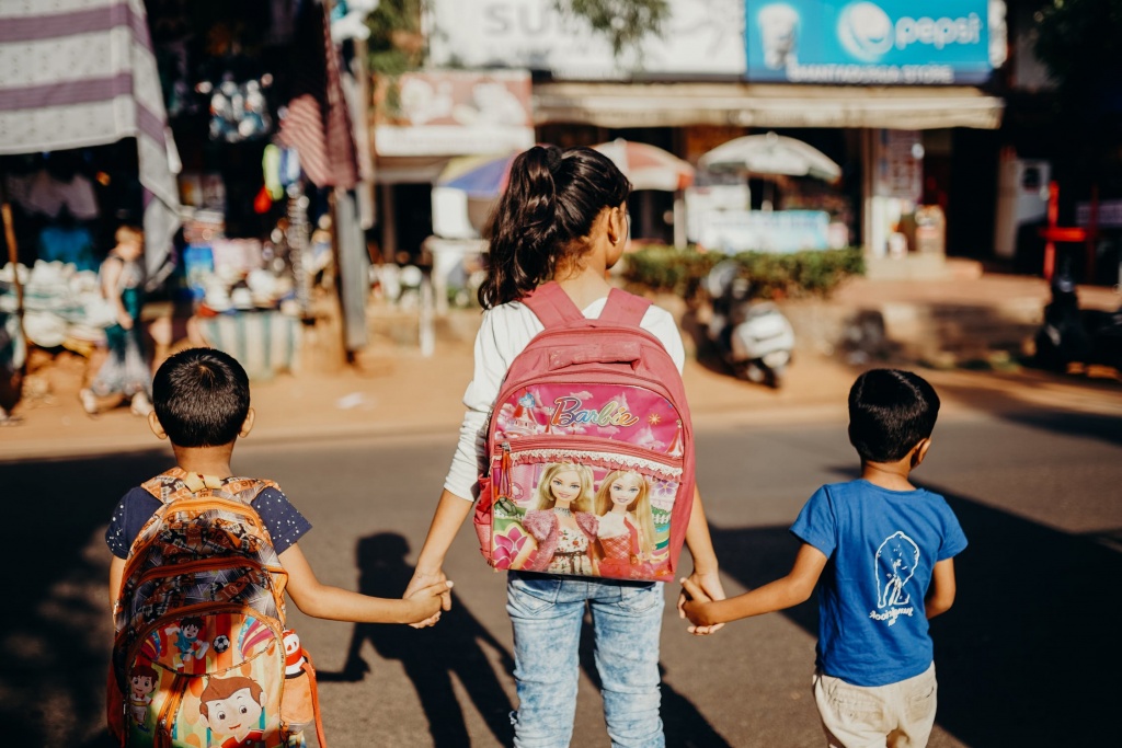 3 kids hold hands with backpacks 